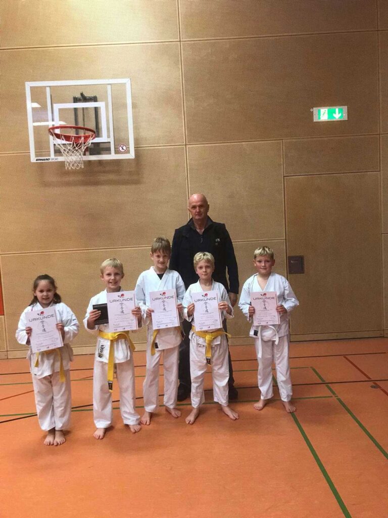 Eine Gruppe von Kindern in weißen Karateanzügen hält Zertifikate.