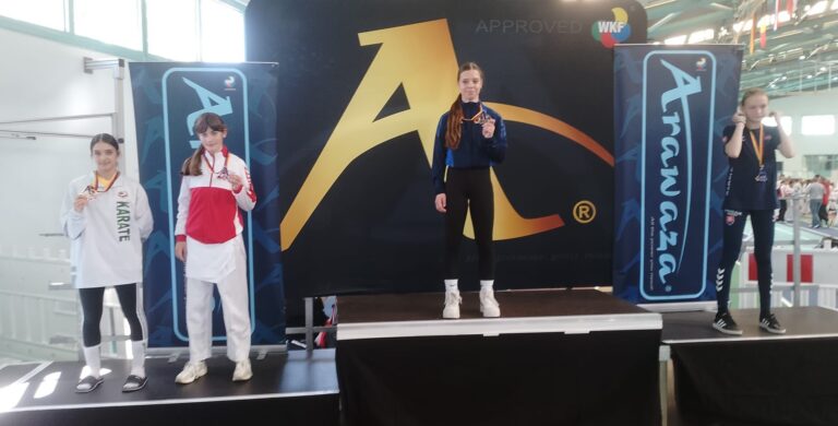 Drei junge Frauen auf einem Siegerpodest, lächelnd, in Sportkleidung mit Medaillen.