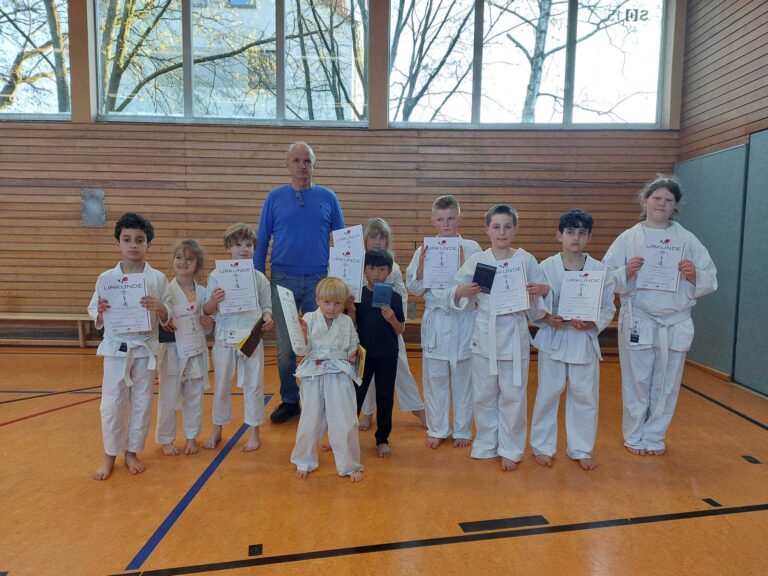 Kinder und ein Erwachsener zeigen stolz Urkunden in einer Turnhalle.