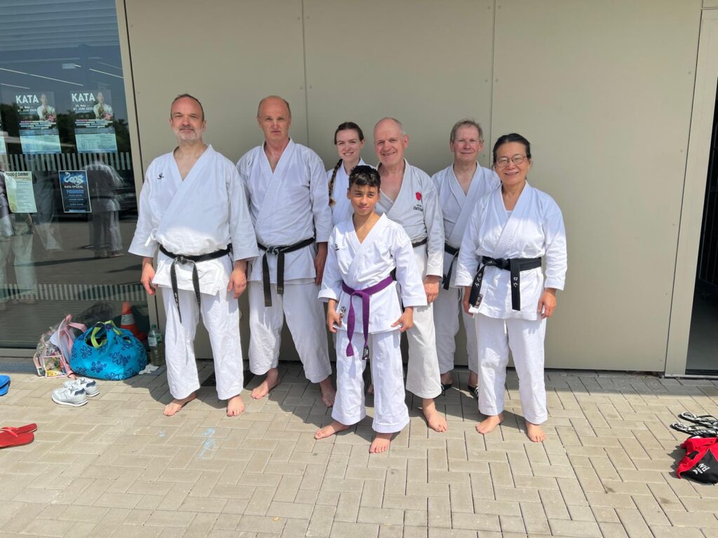 Gruppe von Karateka in weißen Gi mit farbigen Gürtel vor Gebäude, die fröhlich schauen.
