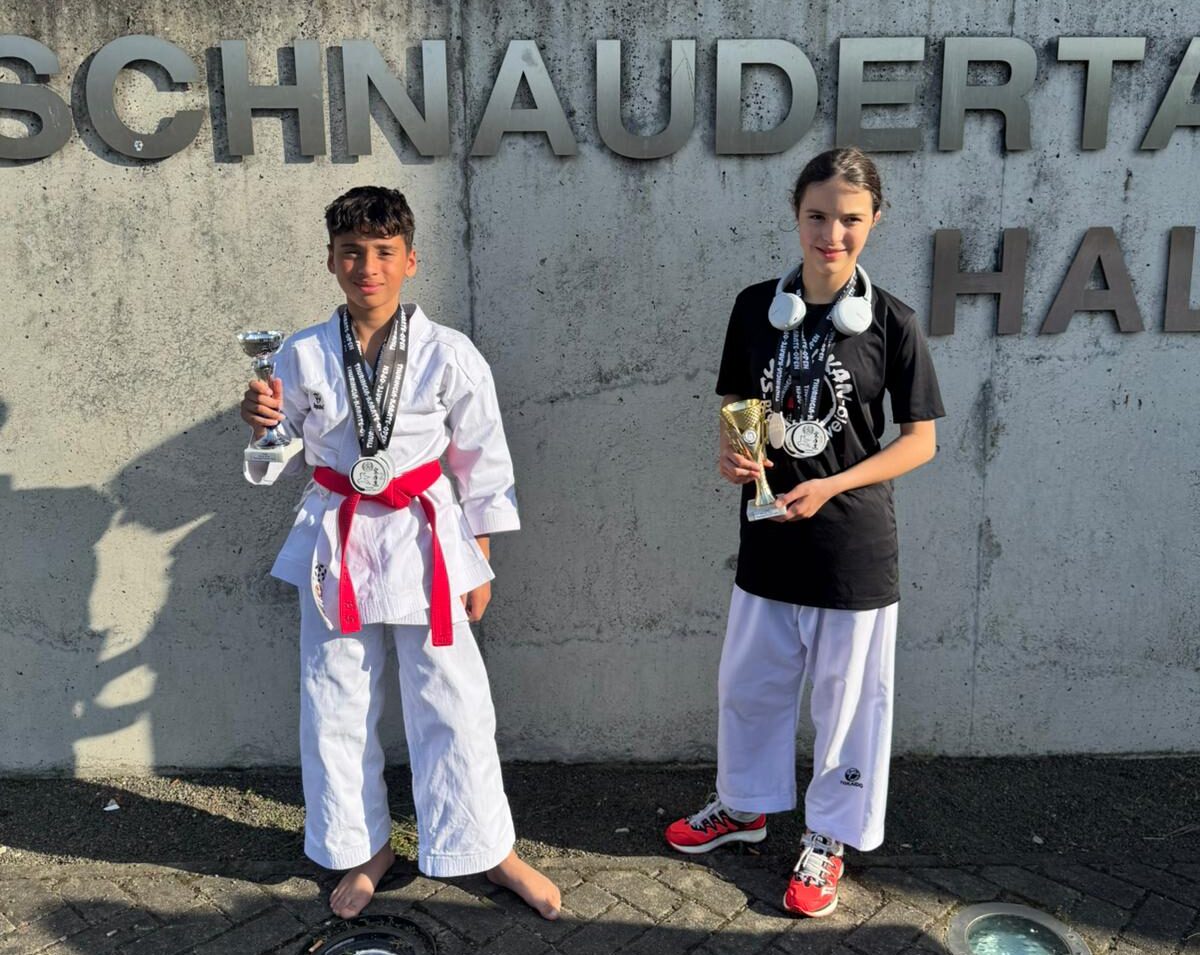 Zwei junge Sportler: Einer im Karateanzug mit Trophäe, der andere in Freizeitkleidung mit Medaille.