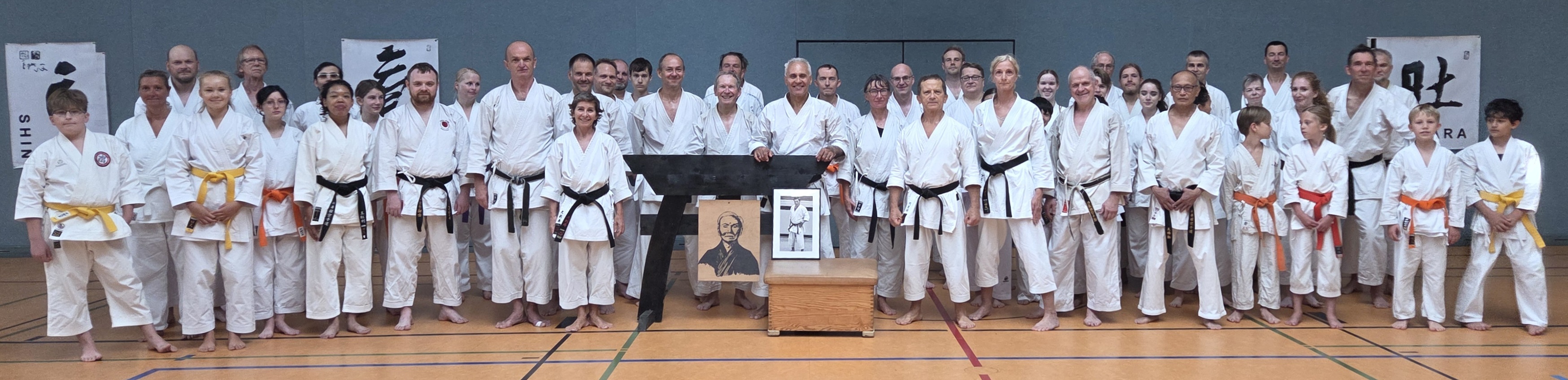 Eine Gruppe lächelnder Menschen in weißen Karate-Gi in einem Dojo.