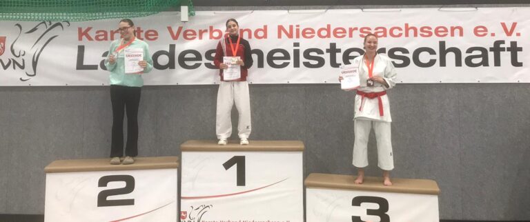 Drei Personen stehen auf einem Siegerpodest bei einer Karate-Veranstaltung.