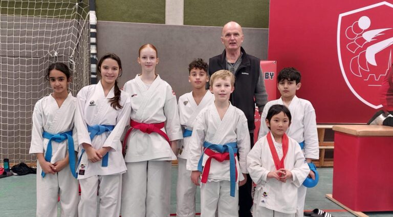 Acht Kinder in weißen Karategis stehen lächelnd neben einem älteren Mann im Anzug