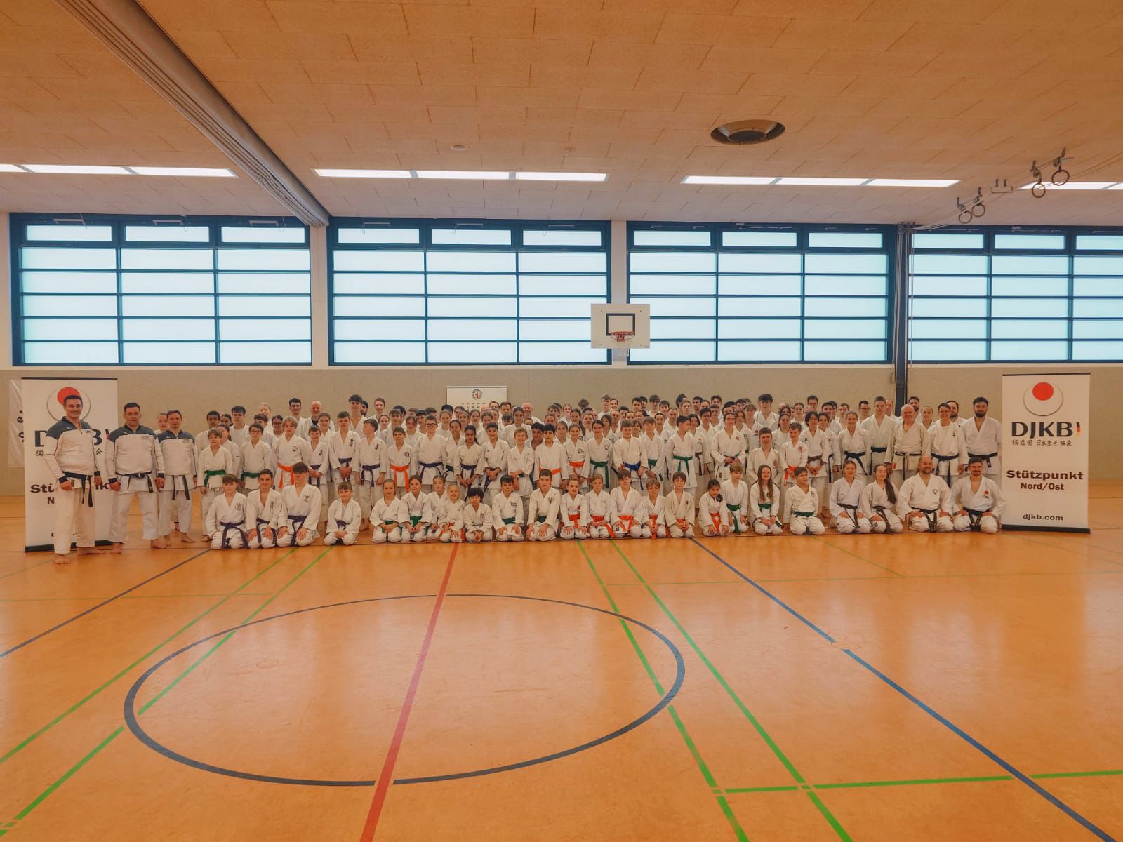 Eine große Gruppe Judoka in weißen Anzügen posiert lächelnd in einer Sporthalle