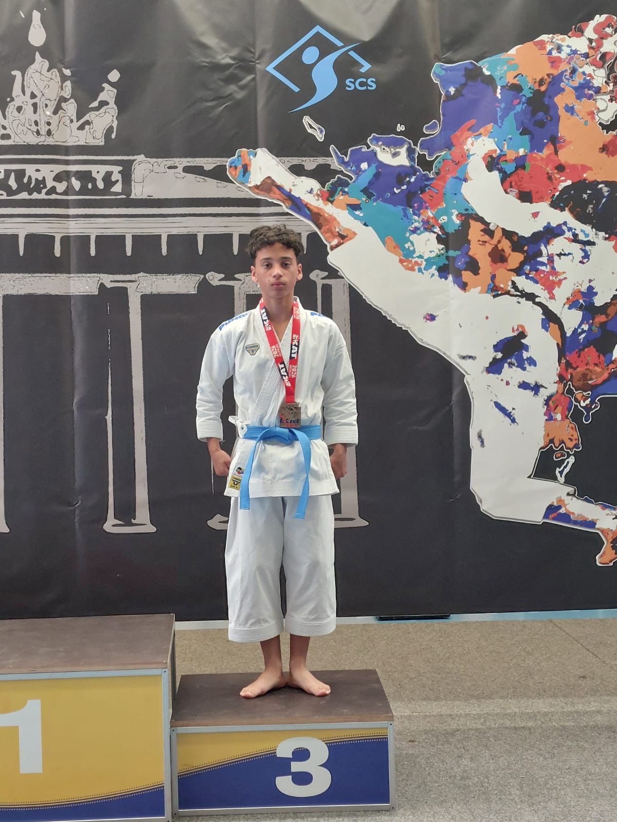 Junger Mann im Karate-Anzug steht ernst mit Medaille auf dem dritten Podestplatz