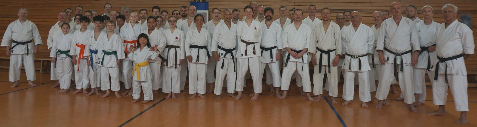 Eine Gruppe von Menschen in weißen Karateanzügen steht lachend in einer Sporthalle