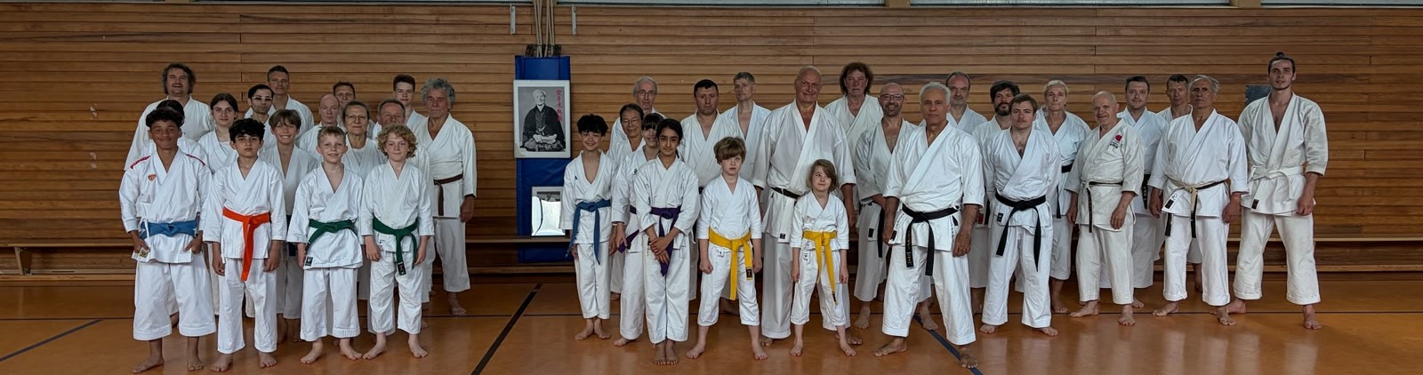 Lachende Karategruppe in weißen Gi mit bunten Gürteln in Turnhalle