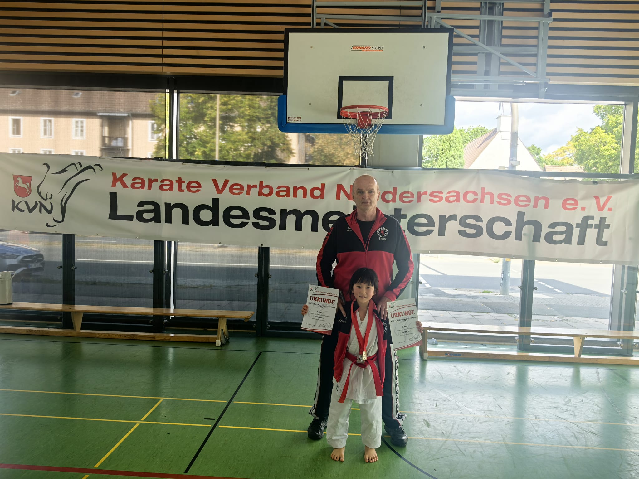Trainer und stolzes Kind mit Medaille und Urkunde bei Karatemeisterschaft