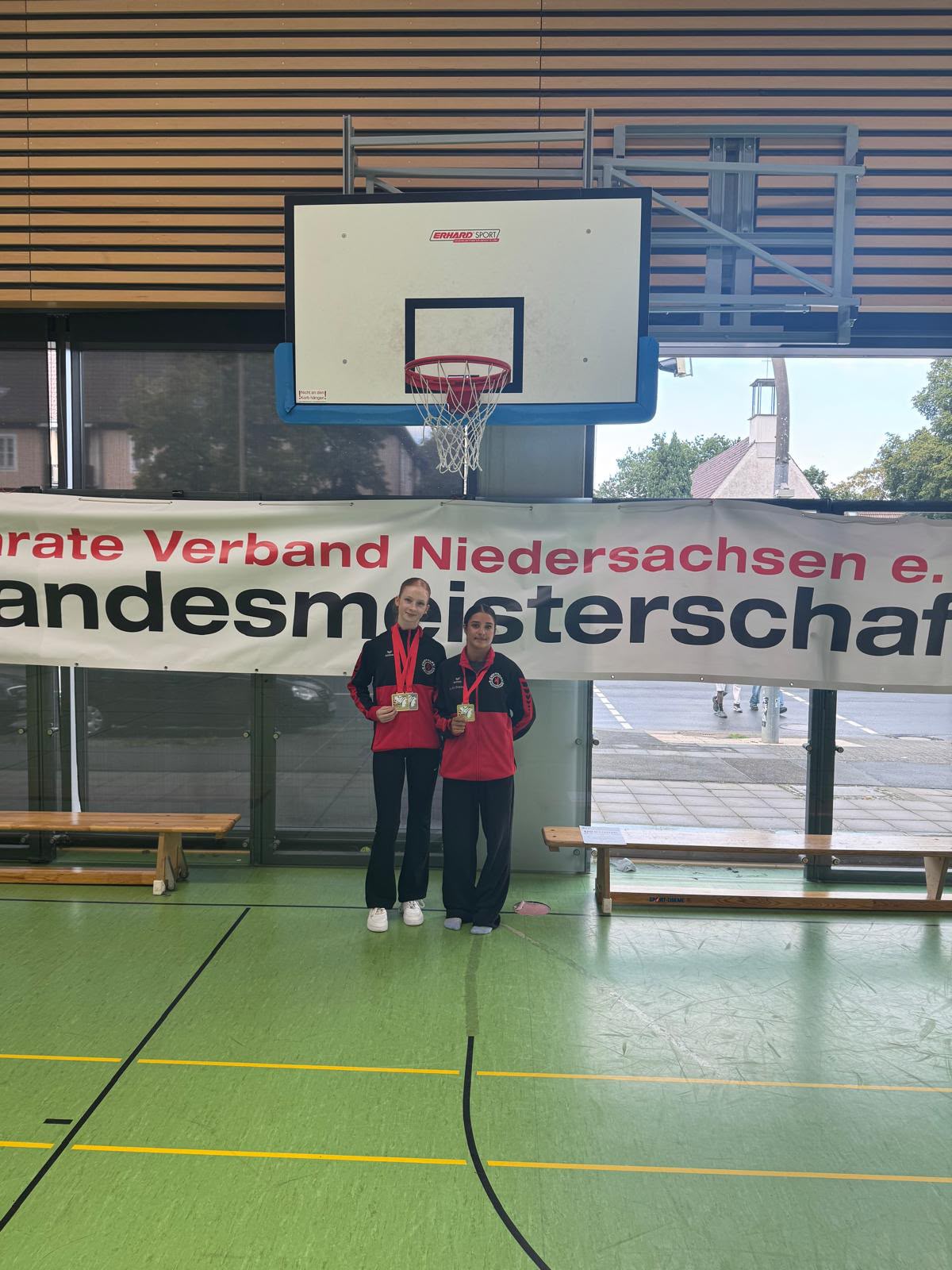 Zwei laechelnde junge Frauen in rot schwarzen Trainingsjacken zeigen stolz Medaillen