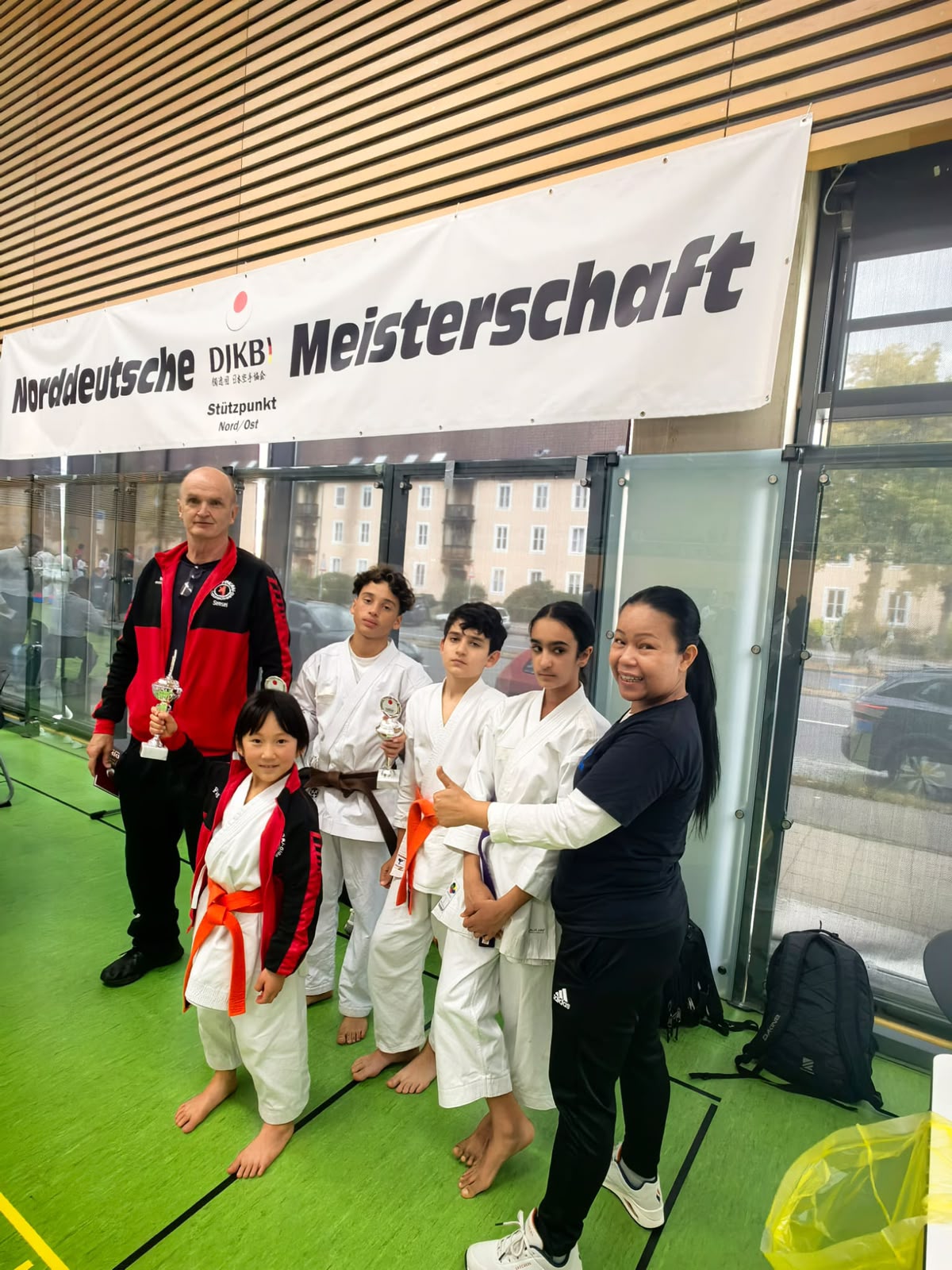 Eine stolze Karategruppe mit Kindern und Trainern haelt Pokale bei der Meisterschaft