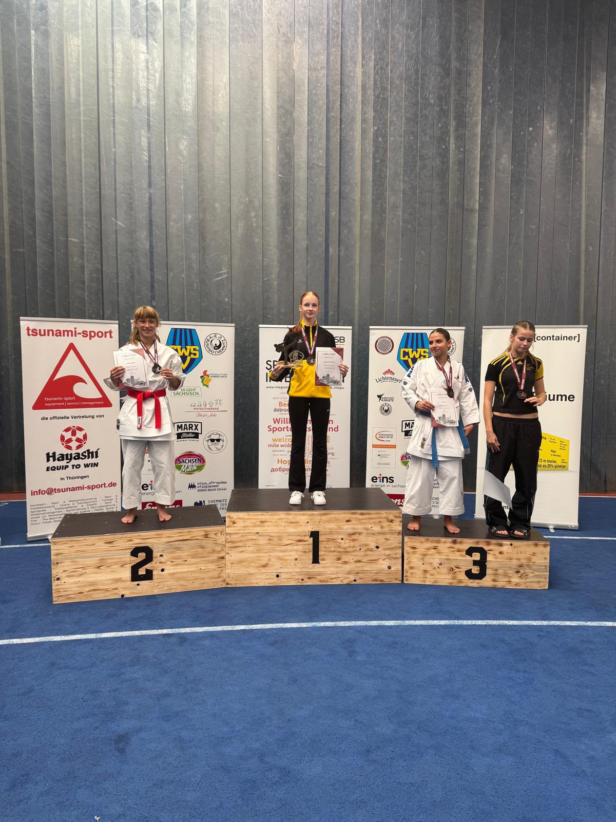 Vier junge Karatesportlerinnen stehen stolz mit Medaillen auf dem Siegerpodest
